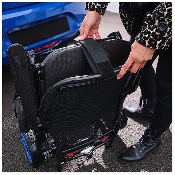 Hands fastening the black transport strap around the folded wheelchair