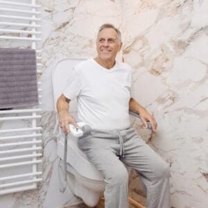 Older man sitting on the tilting toilet seat holding the remote control
